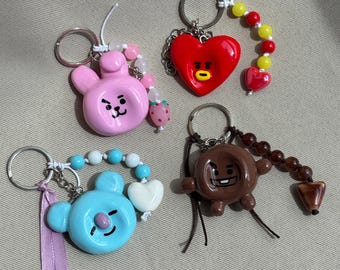 May include: Four character keychains featuring a pink rabbit, a red heart, a light blue bear, and a brown creature. Each keychain includes a metal ring, colourful beads, and small charms like a strawberry, hearts, and a lavender ribbon.
