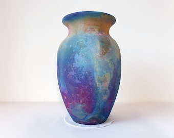 May include: A ceramic vase with a blue, purple, and green iridescent glaze. The vase has a rounded body and a wide mouth.