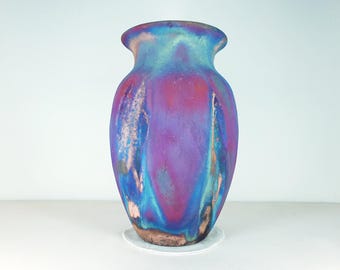 May include: A ceramic vase with a iridescent glaze in shades of blue, purple, and pink. The vase has a rounded body and a flared lip.