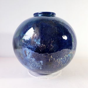 Könnte beinhalten: Eine runde, blaue Keramikvase mit einem gesprenkelten, irisierenden Überzug. Die Vase hat eine breite Öffnung und einen abgerundeten Boden.