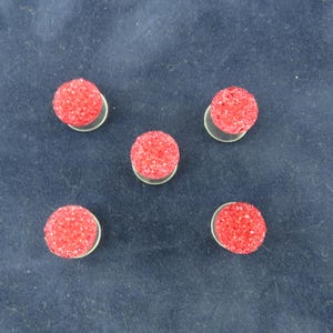 May include: Five red, round, textured, decorative embellishments with a white backing.