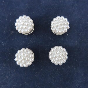 May include: Four white pearl cluster buttons on a dark blue background. Each button is composed of numerous small, round pearls arranged in a floral pattern. The buttons have a silver backing.
