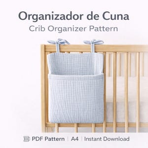 Puede incluir: Un patrón de organizador de cuna azul claro colgado de una cuna de madera. El organizador tiene un bolsillo y se sujeta con lazos de tela. El texto "Organizador de Cuna" y "Crib Organizer Pattern" están en la parte superior. El texto inferior dice "PDF Pattern", "A4" e "Instant Download".
