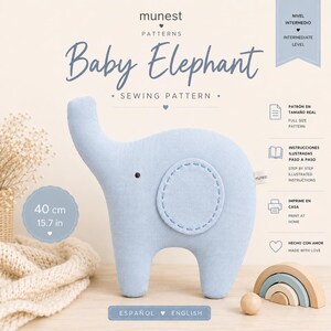 May include: A light blue fabric baby elephant sewing pattern by Munest. The design features a rounded body, a single visible ear with stitched detailing, and a small dark eye. Text includes Baby Elephant, 40 cm, 15.7 in, and instructions.