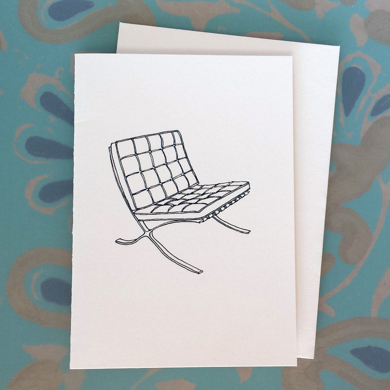 May include: A black and white line drawing of a modern chair on a white card. The chair features a grid-like seat and back, with a curved metal frame. The card is paired with a blank white envelope.
