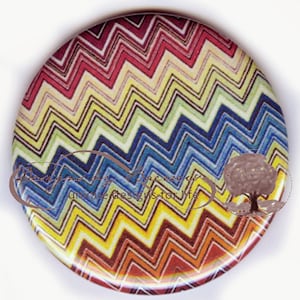 May include: A round decorative item with a colorful zigzag pattern in shades of red, yellow, blue, and green. The item has text that reads "Baeckcks unique designs for life" and a tree graphic.