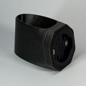 Könnte beinhalten: Schwarzer Fahrradhalter aus Kunststoff mit sechseckiger Form und einer kleinen runden Öffnung mit einem G-Logo.