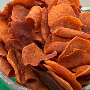 May include: A bowl of crispy, golden brown sweet potato chips. The chips are piled high in the bowl and have a slightly caramelized appearance.