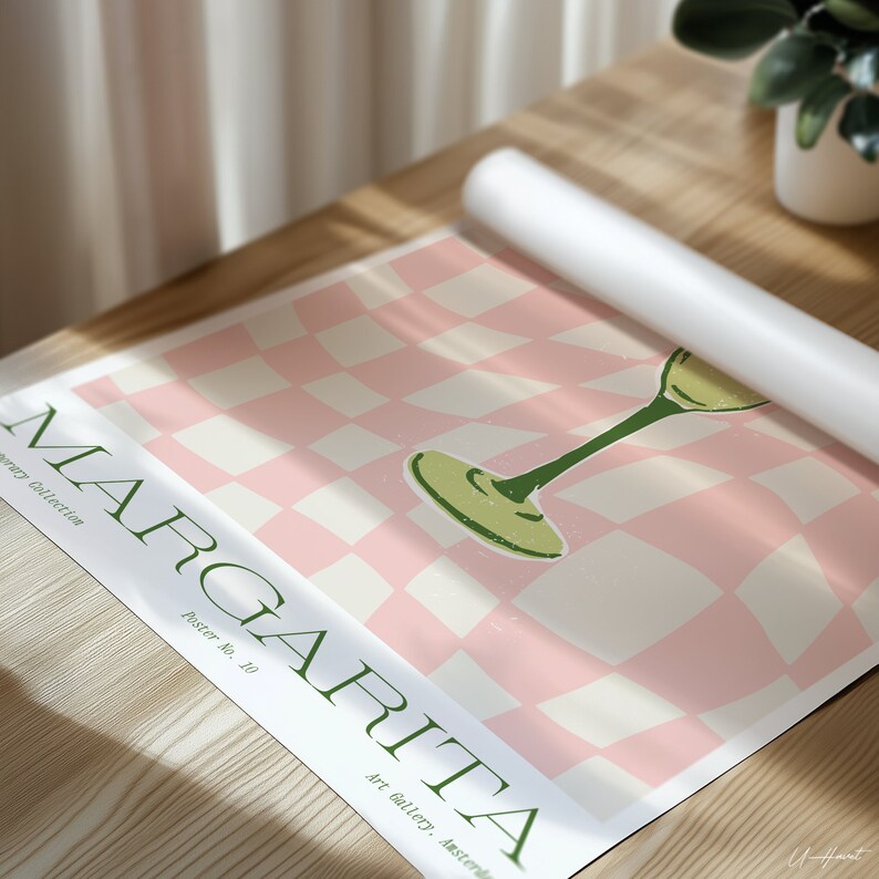 May include: A rolled-up poster featuring a margarita glass illustration on a pink and white checkered background. The poster has the word "MARGARITA" in green, with "Poster No. 10" and "Art gallery, Amsterdam" printed below. The poster is on a wooden surface.