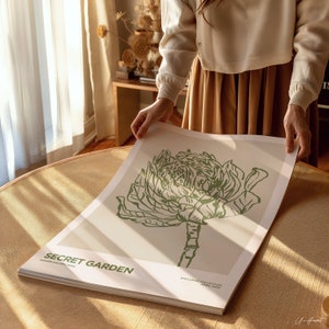 Op de afbeelding: Een witte poster met een groene lijntekening van een bloem op een beige achtergrond. De poster heeft de tekst "SECRET GARDEN" en "FLOWER GALLERY PARIS" in de linkerbenedenhoek. De tekst "EXCLUSIVE COLLECTION" en "APRIL 2023" staat in de rechterbenedenhoek.