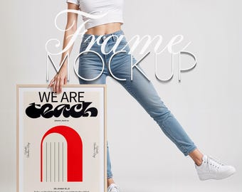 May include: A framed poster with the words "WE ARE teach" in black, with a red arch design. The poster is held by a person wearing a white top and blue jeans. The frame is light brown.