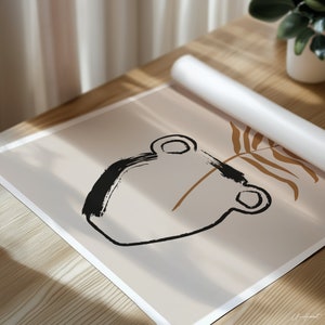 May include: An abstract art print featuring a black brushstroke design of a vase with a brown stem and leaf on a beige background. The print is partially rolled up, resting on a wooden surface, with a white roll of paper and a potted plant in the background.