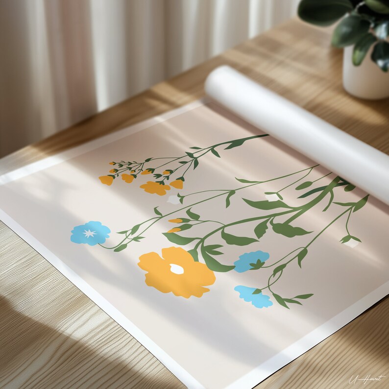 May include: A floral art print featuring a bouquet of stylized flowers in yellow and blue against a light beige background. Green stems and leaves complement the blooms. A rolled-up white poster is partially visible. The artwork is on a wooden surface.