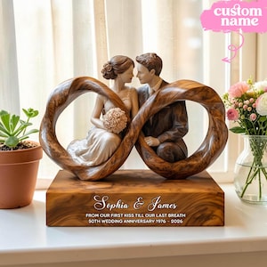 Puede incluir: Una escultura de aniversario de bodas de madera con una pareja dentro de un símbolo de infinito. La base está grabada con los nombres "Sophia & James" y el texto "From our first kiss till our last breath 50th wedding anniversary 1976-2026".