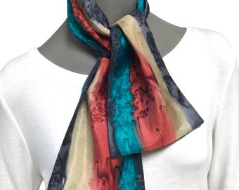 May include: A colorful scarf with a vertical striped pattern in shades of teal, red, beige, and gray. The scarf is knotted at the neck, showcasing the vibrant color palette and fluid design. The scarf appears to be made of a silky material.