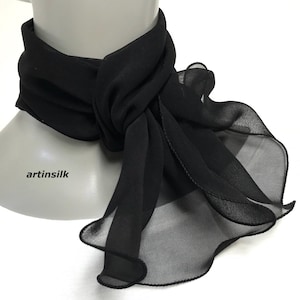 May include: A black sheer scarf with a ruffled edge. The scarf is tied around a mannequin's neck and the ends are draped down the front of the mannequin.