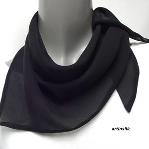 May include: A black chiffon scarf with a simple design. The scarf is folded and draped around a mannequin's neck. The brand name "artinsilk" is printed on the white background.