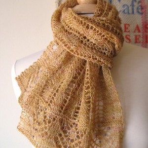 May include: A delicate, crocheted scarf in a warm, golden brown color with a lacy pattern. The scarf is adorned with small, pearl-like beads.