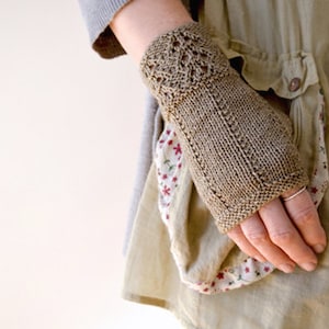 May include: A close-up of a person wearing a brown knitted fingerless glove with a delicate lace pattern. The glove is worn on the left hand and the person is wearing a light brown dress.