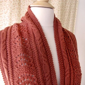 May include: A rust-colored knitted scarf with a cable knit pattern. The scarf is made of soft yarn and has a delicate, lacy design.