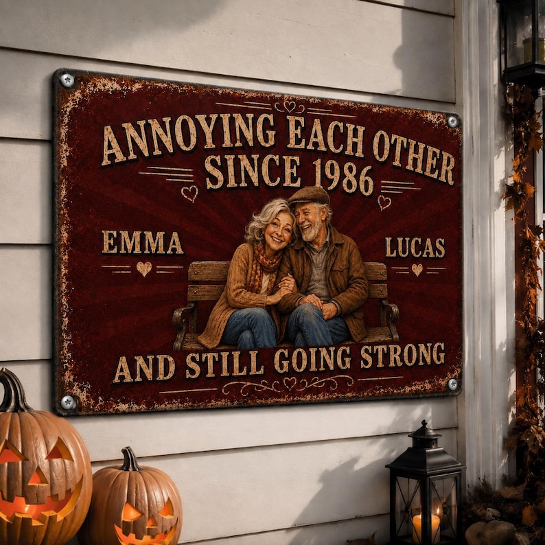 K&ouml;nnte beinhalten: Ein rechteckiges Metallschild mit einem abgenutzten dunkelroten Hintergrund und einer Illustration eines &auml;lteren Paares auf einer Bank. Der Text lautet: ANNOYING EACH OTHER SINCE 1986, EMMA, LUCAS, AND STILL GOING STRONG, mit kleinen Herzsymbolen.