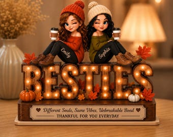 May include: A decorative wooden sign featuring the word BESTIES illuminated by small lights, topped with two figurines wearing beanies and holding coffee cups. The base displays the text: Different Souls, Same Vibes, Unbreakable Bond THANKFUL FOR YOU EVERYDAY.