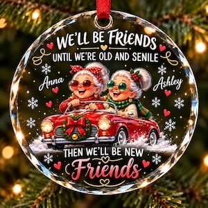 May include: A round, clear acrylic Christmas ornament featuring two elderly characters in a red convertible car. The text reads: WE'LL BE FRIENDS UNTIL WE'RE OLD AND SENILE THEN WE'LL BE NEW FRIENDS, with the names Anna and Ashley printed on the sides.