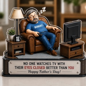 May include: A decorative figurine featuring a man asleep in a brown armchair, holding a remote control. A small table with a lamp and a mug that says "BEST. DAD. EVER." is next to him. The base reads "NO ONE WATCHES TV WITH THEIR EYES CLOSED BETTER THAN YOU Happy Father's Day!"