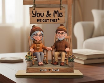 May include: A decorative figurine featuring an elderly couple in rocking chairs, holding hands. The sign above them reads "You & Me WE GOT THIS". The base is engraved with "Sarah ♥ David". The couple is wearing hats and sweaters.