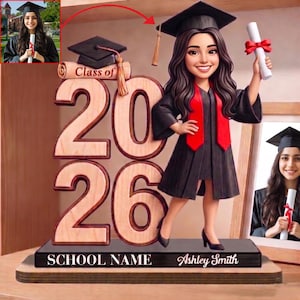 May include: A graduation-themed wooden figurine featuring a smiling graduate in a cap and gown, holding a diploma with a red ribbon. The base displays the school name and graduate's name, with the year "2026" prominently displayed.