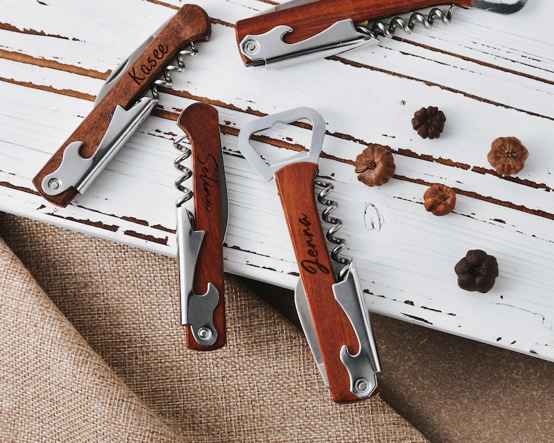 May include: Four wooden bottle openers with personalized names, "Kasee", "Selena", "Jenn", and an unreadable name. The openers have a corkscrew, bottle opener, and a small knife.