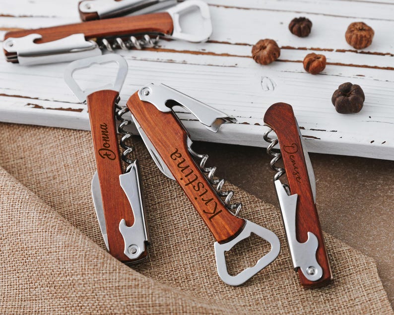 May include: Three personalized wooden bottle openers with corkscrews. The bottle openers are engraved with the names "Donna", "Kristine", and "Denise".