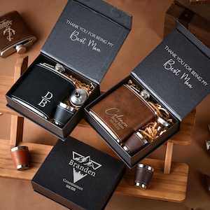 Pode incluir: Conjuntos de presente com frascos e copos de shot. Um conjunto inclui um frasco preto com iniciais, e outro um frasco castanho com um nome e uma data. As caixas dizem "THANK YOU FOR BEING MY Best Man" e "Branden Groomsman Estd 2015".