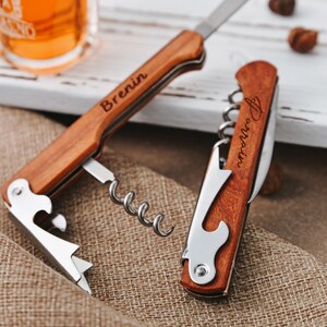 May include: A wooden bottle opener with a corkscrew, bottle opener, and knife. The opener is engraved with the name "Brenin".