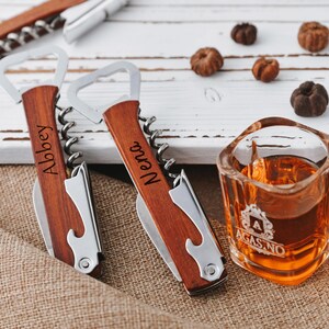 May include: Two wooden handled bottle openers with corkscrews. The handles are engraved with the names "Abbey" and "Nena".