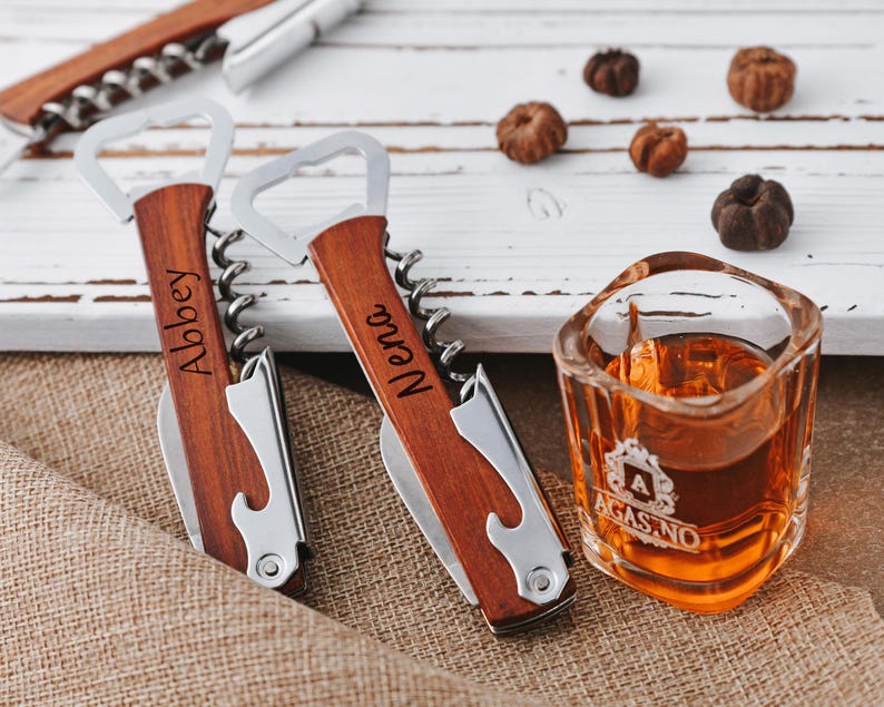 May include: Two wooden handled bottle openers with corkscrews. The handles are engraved with the names "Abbey" and "Nena".