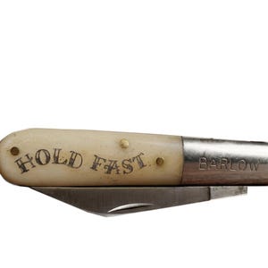 May include: A vintage Barlow pocket knife with a cream-colored handle and a silver blade. The handle is inscribed with "HOLD FAST" in black lettering. The blade is folded into the handle. The word "BARLOW" is stamped on the silver end.