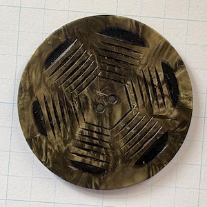 May include: A round, olive-green button with a geometric design. The button features a series of carved lines and shapes, creating a textured surface. Two small holes are visible in the center for sewing. The button is likely made of a durable material.
