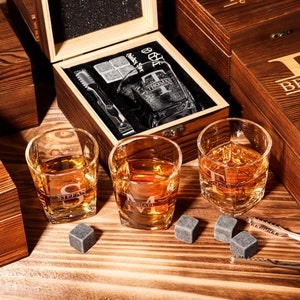 Puede incluir: Un juego de tres vasos de whisky personalizados con una caja de madera, piedras de whisky y unas pinzas. Los vasos están grabados con los nombres "Stefan", "Michael" y "Thomas". La caja está grabada con el nombre "Brandon".