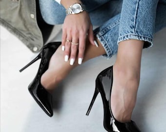 May include: Pair of glossy black stiletto heels with pointed toes. The shoes have a high heel and a sleek, polished finish. The heels are a classic style, suitable for formal occasions or adding a touch of elegance to any outfit.