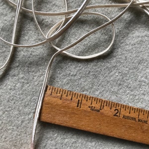 Pode incluir: Um close-up de um cord&atilde;o ou fita de cetim branco, medido com uma r&eacute;gua de madeira. A r&eacute;gua &eacute; marcada em polegadas e com o texto "Falcon" e "Auburn, Maine".