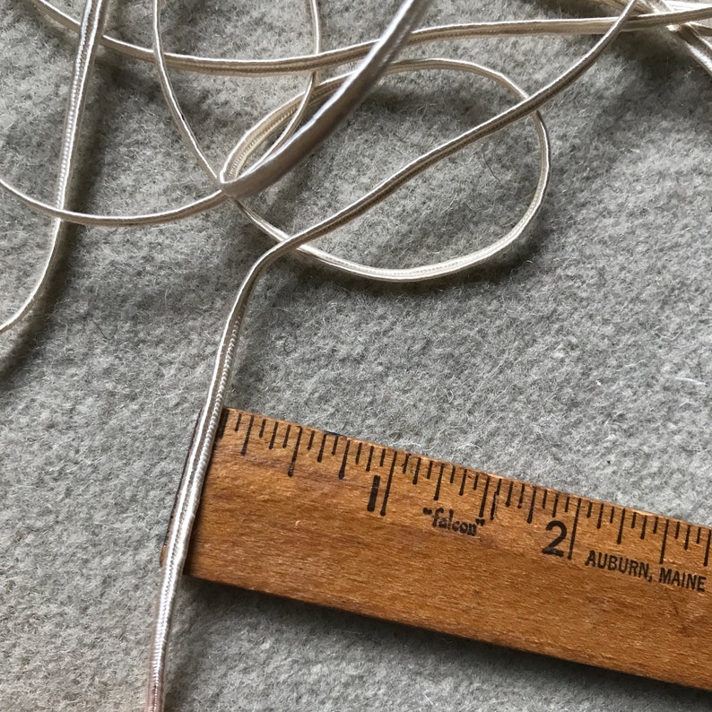 Pode incluir: Um close-up de um cord&atilde;o ou fita de cetim branco, medido com uma r&eacute;gua de madeira. A r&eacute;gua &eacute; marcada em polegadas e com o texto "Falcon" e "Auburn, Maine".