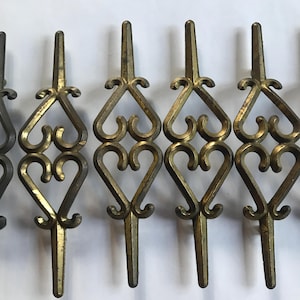 May include: Six gold-toned metal drawer pulls with a decorative heart design. The pulls have a pointed tip and a decorative scroll design.