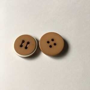 May include: Two brown plastic buttons, one with two holes and a white rim, the other with four holes.