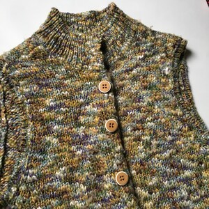 May include: A sleeveless knitted vest with a high neck and a multi-colored striped pattern. The vest has three brown buttons down the front.