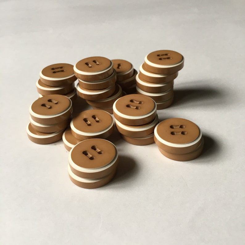 May include: A pile of brown buttons with a white rim. The buttons have two holes each.