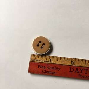 May include: A brown two-hole button with a white rim. The button is approximately 1 inch in diameter.