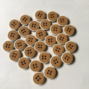 May include: A collection of 22 brown buttons with white trim and two holes each. The buttons are arranged in a circle on a white background.