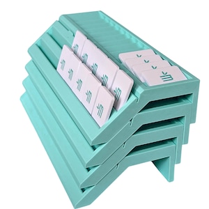 May include: A stack of four light mint green plastic card holders with angled slots. Each holder contains several white rectangular cards featuring a small teal leaf icon and a stylized letter M printed on the front surface of each card.