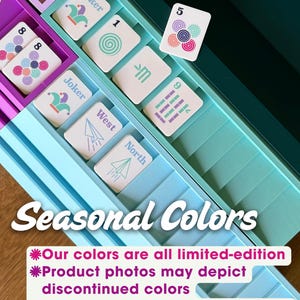 May include: A multi-colored plastic game card organizer tray with various compartments containing playing cards featuring Joker, number, and directional symbols. The text Seasonal Colors and a disclaimer about limited-edition colors are visible.